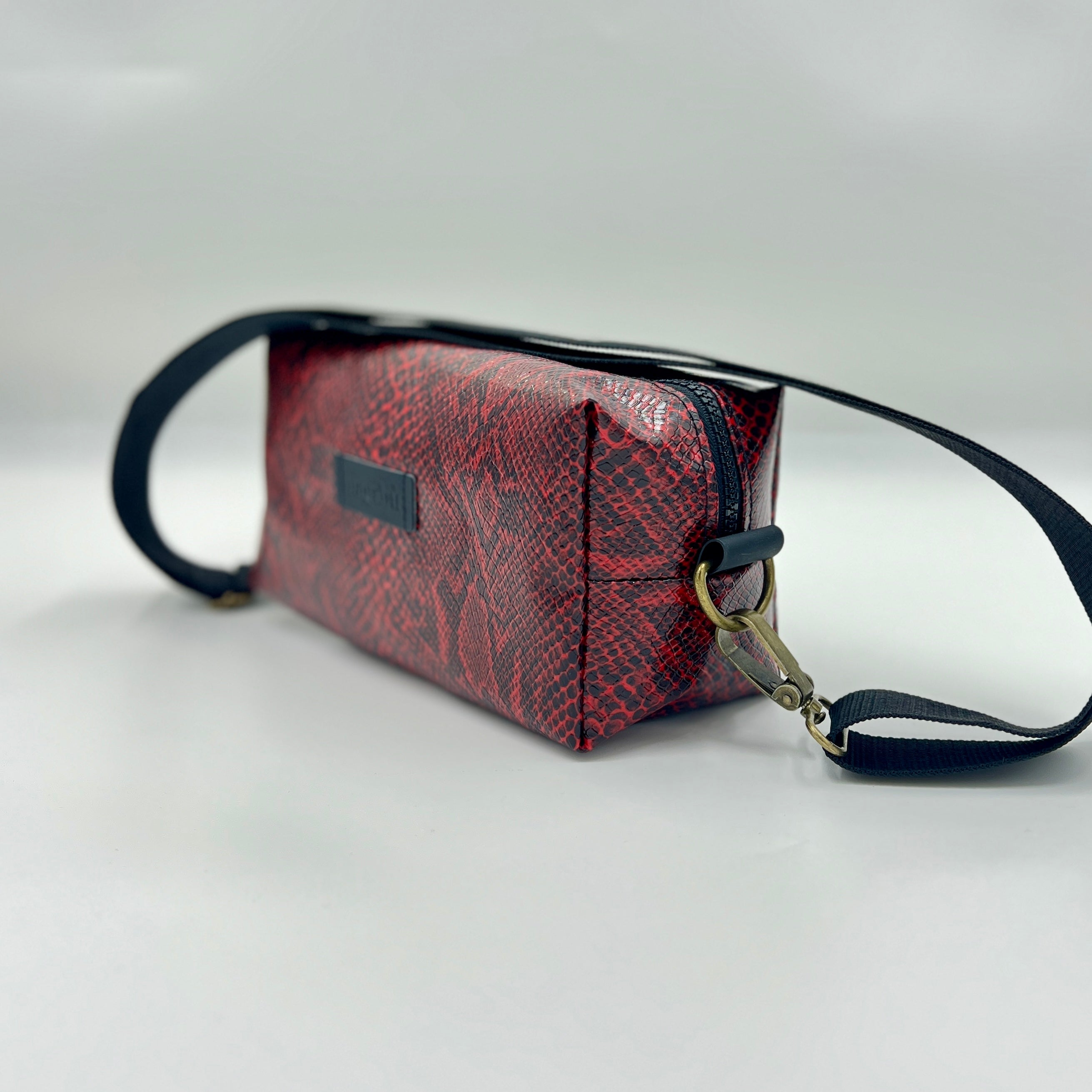Red textured handbag with black strap on a light gray background