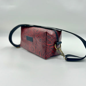 Red textured handbag with black strap on a light gray background