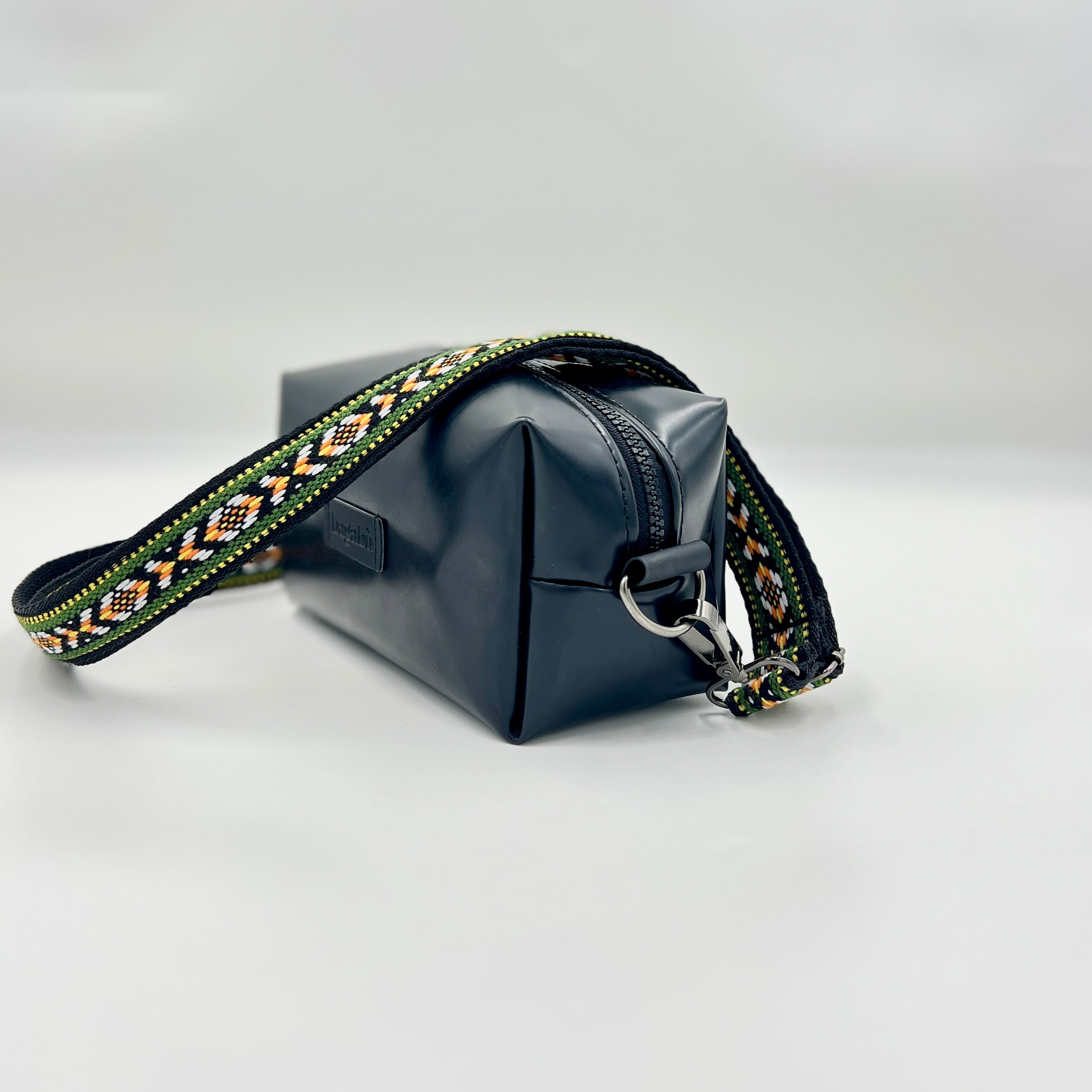 Black leather bag with a patterned strap on a light gray background