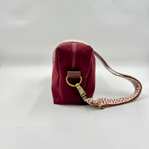 Maroon handbag with a patterned strap on a light gray background
